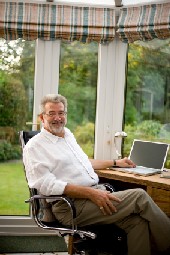 Here's an alt tag for the image: Smiling man working on laptop in sunroom.