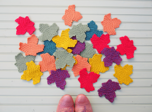 A person standing next to colorful crocheted leaves.