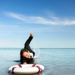 Here's an alt tag for the image: Businesswoman struggling in water, reaching for life preserver.