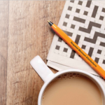 Here's an alt tag for the image: `Coffee, crossword, and pen ready for solving.`